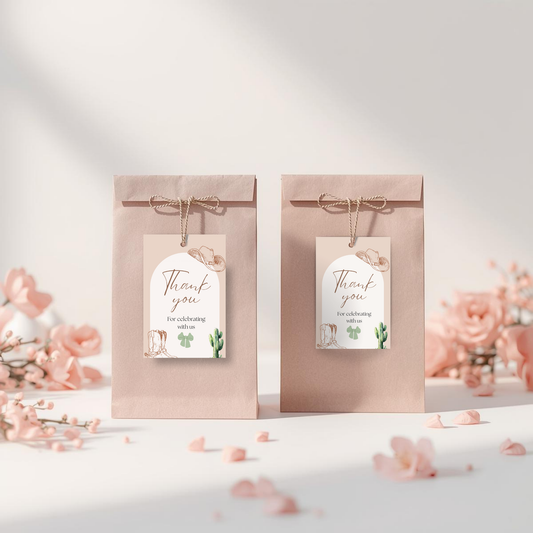 Two blush pink paper gift bags tied with jute twine and decorated with matching 'Thank you' tags, styled on a white surface with scattered pink flower petals and blurred pink roses in the background.
