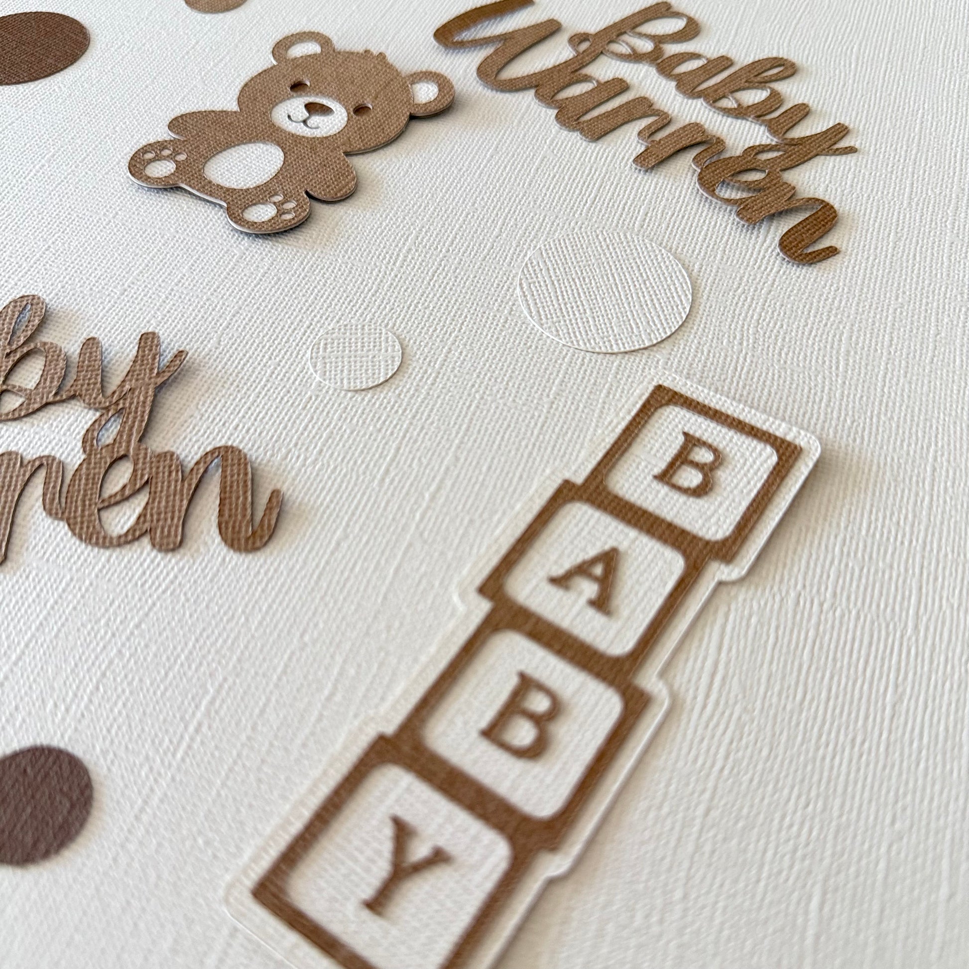 Baby-themed confetti with 'Baby Warren' and teddy bear on a textured beige background.