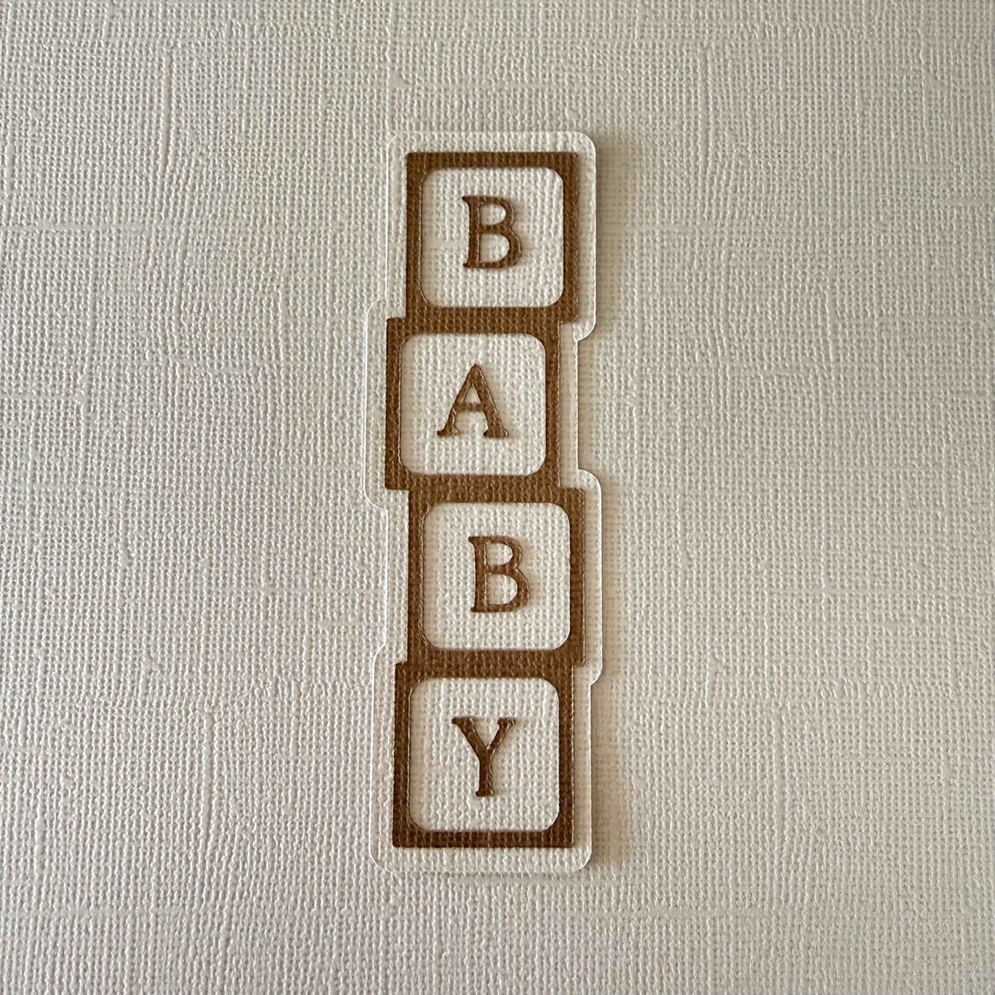 'BABY' block confetti letters on a textured beige background