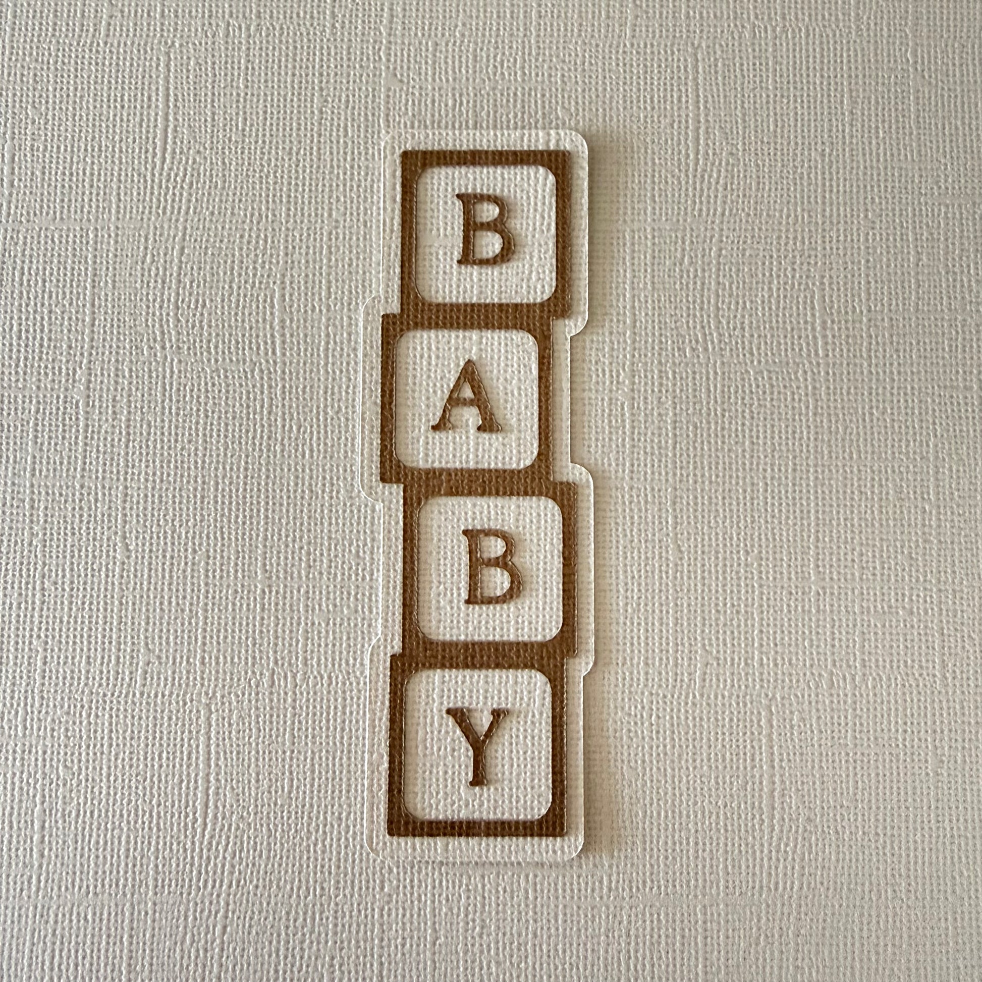 'BABY' block confetti letters on a textured beige background