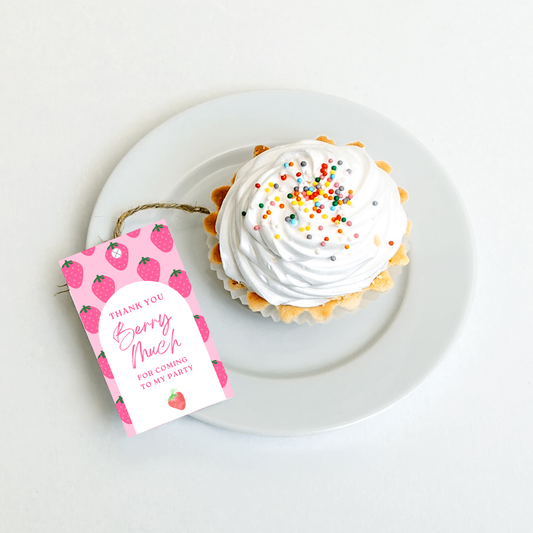 Cupcake with white frosting and colorful sprinkles on a white plate, accompanied by a pink 'Thank You' tag with strawberry design.