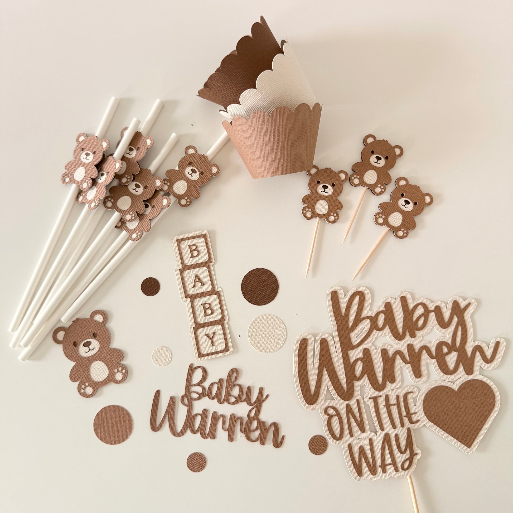 Baby shower decorations with teddy bears, 'Baby Warren' text, and cupcake toppers on a light background.