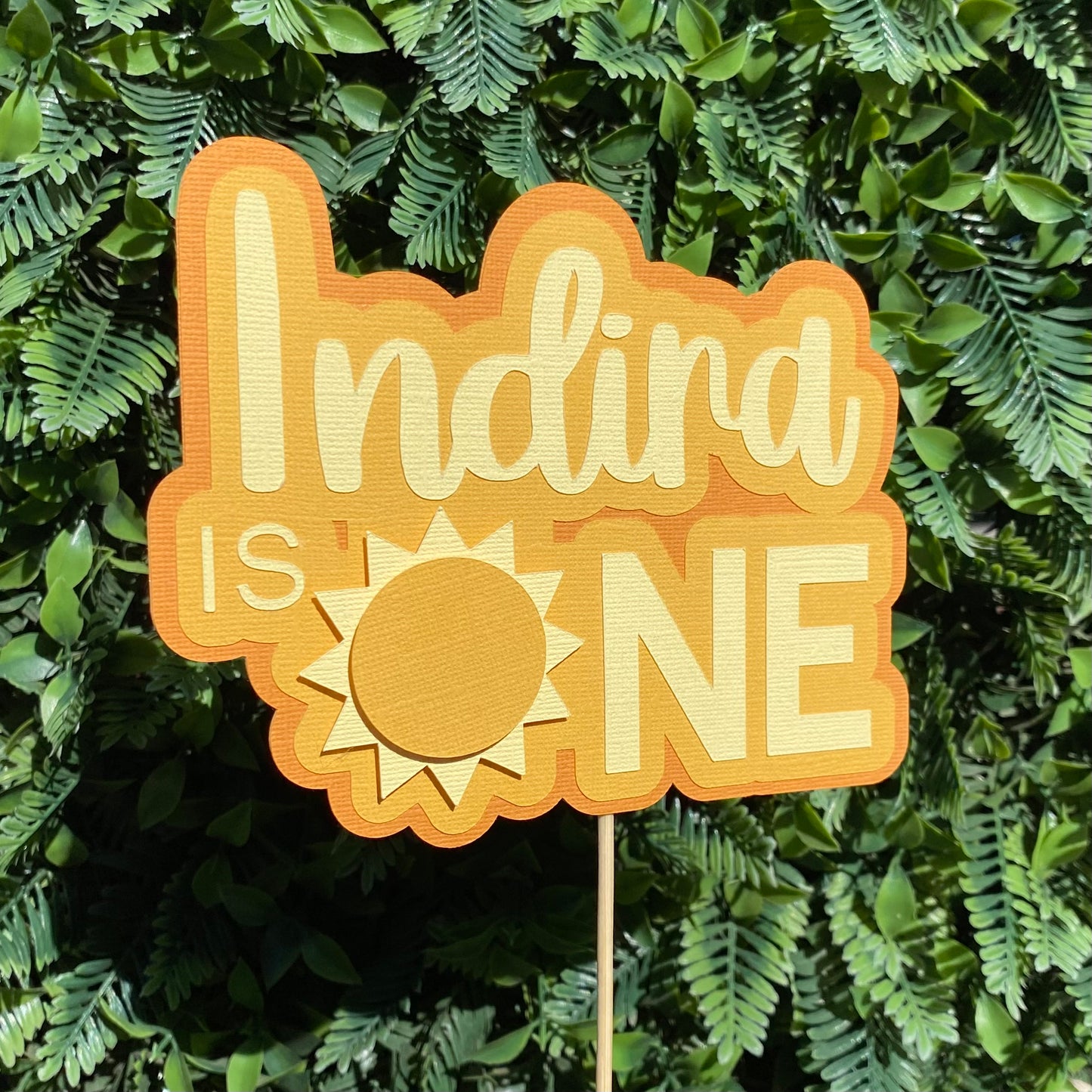 Decorative sign with 'Indira is ONE' on a green leafy background