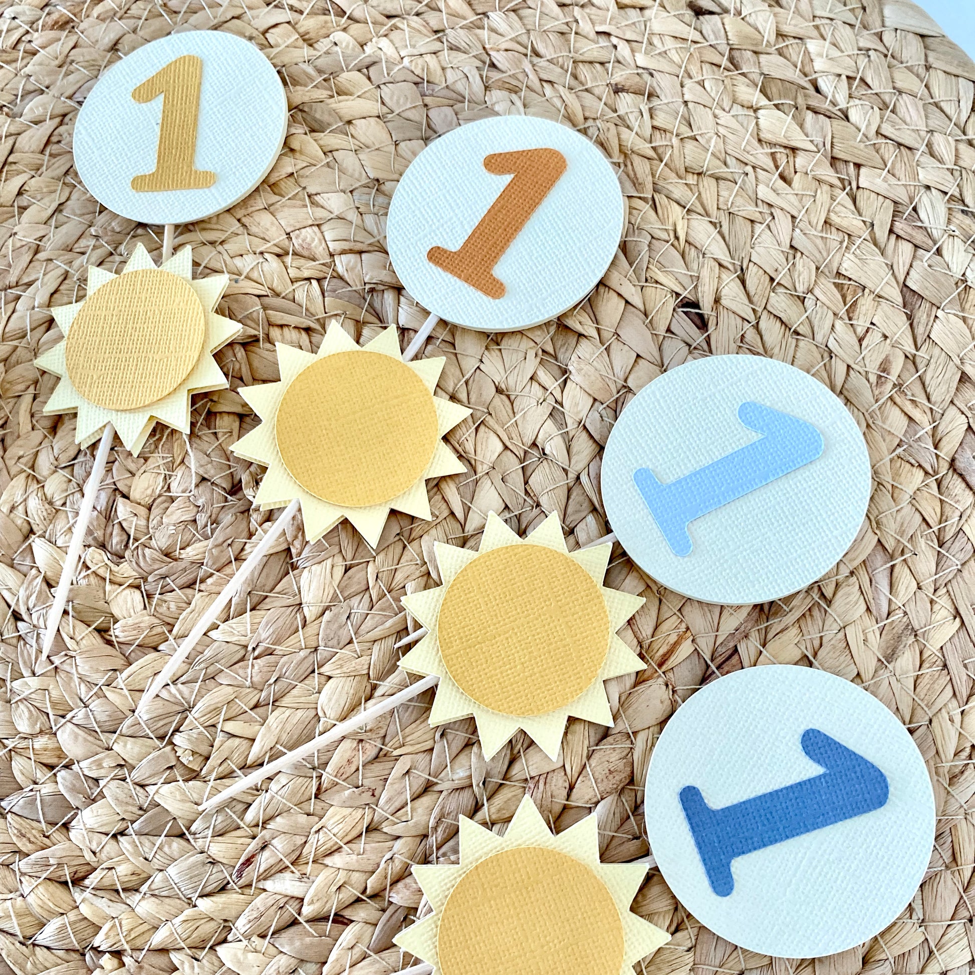 Decorative cupcake toppers with number '1' on a woven surface