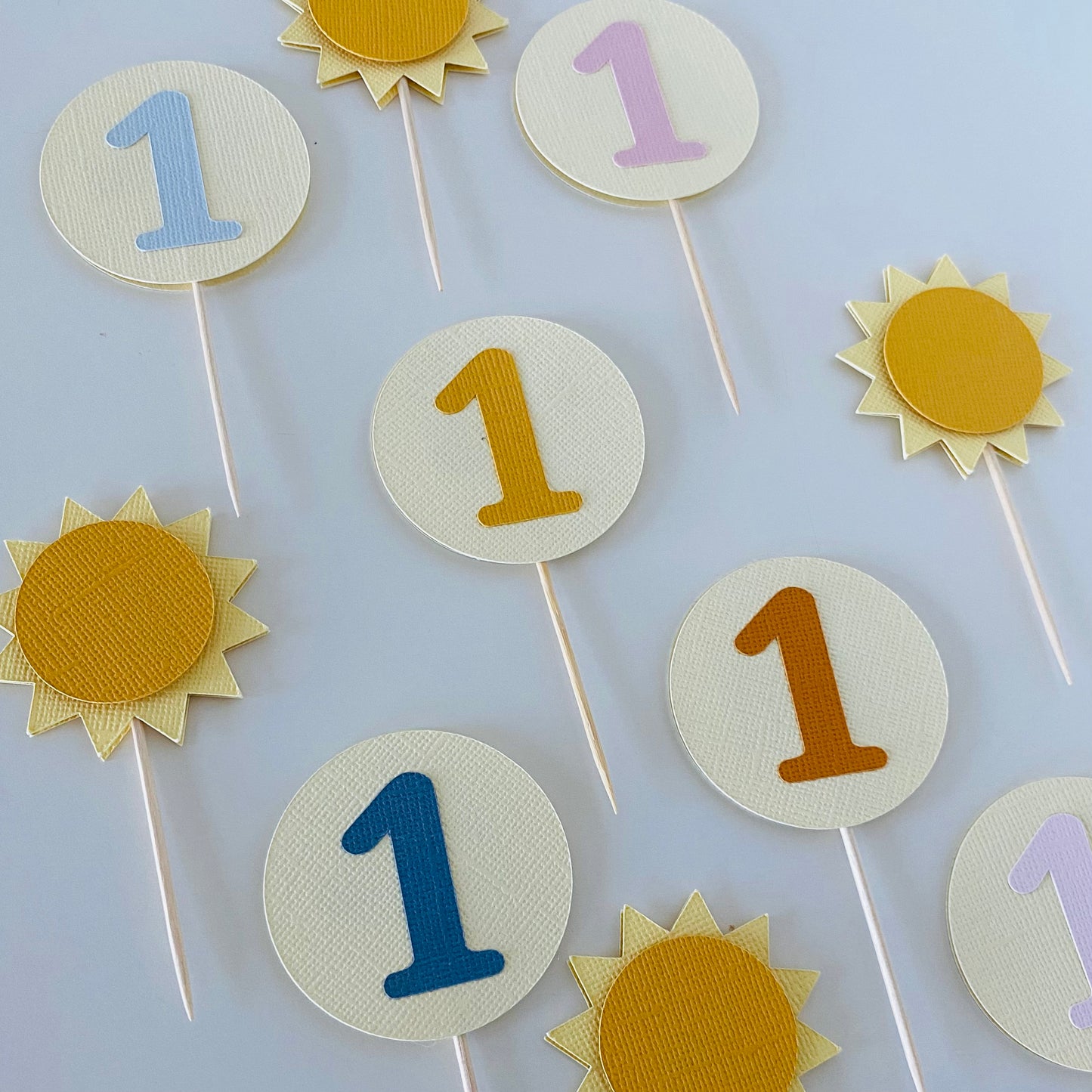 Decorative cake toppers with numbers and sun designs on sticks against a white background.
