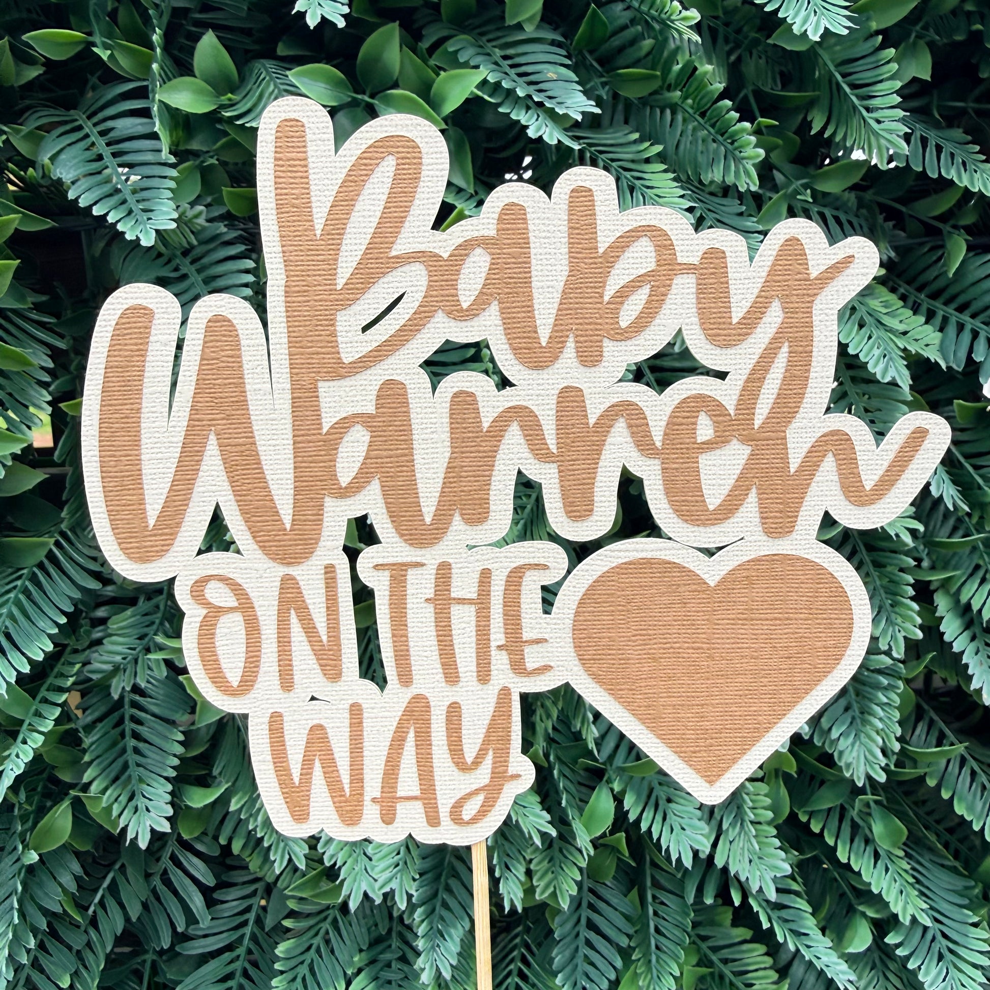 Wooden baby shower sign with 'Baby Warren On The Way' text on a green leafy background