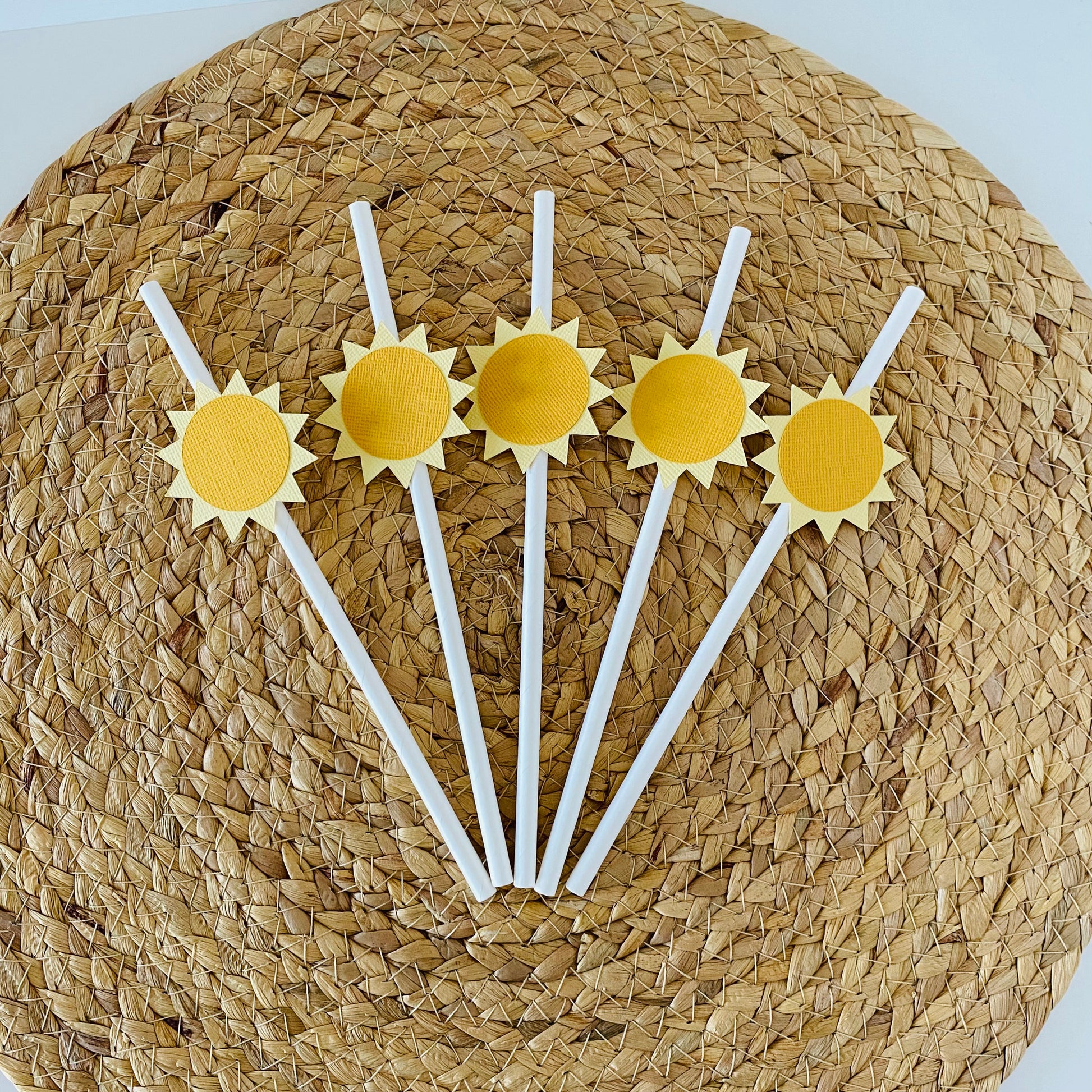 Five yellow sun-shaped straws on a woven mat