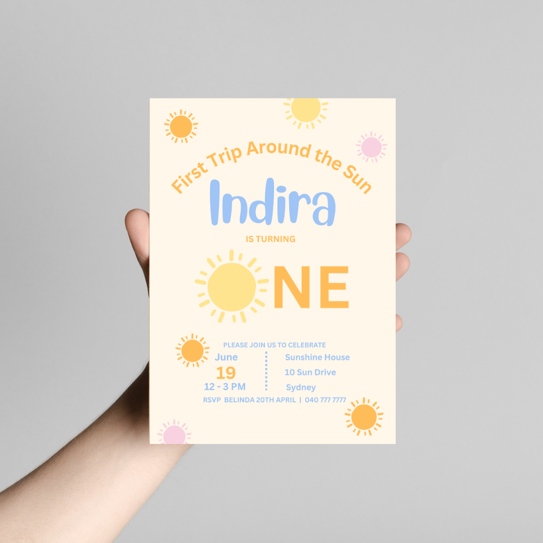 Invitation card for a first birthday party with sun-themed design, held against a gray background.